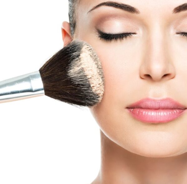 Closeup portrait of a woman  applying dry cosmetic tonal foundation  on the face using makeup brush.